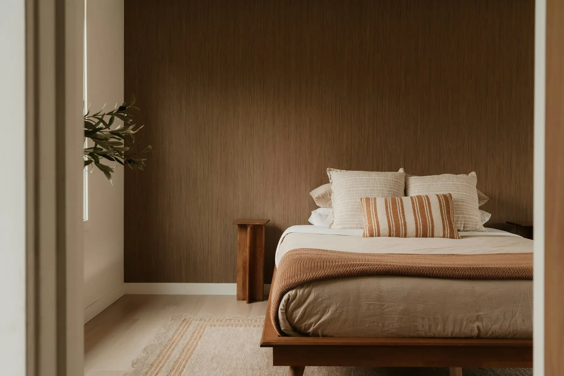 Schlafzimmer mit Holzbett, warmen Stoffen und Holzwand